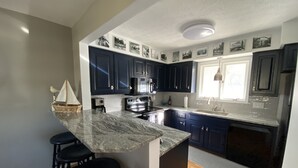 Una cocina moderna con armarios azul oscuro, una isla de mármol con taburetes altos y una isla central con fregadero.