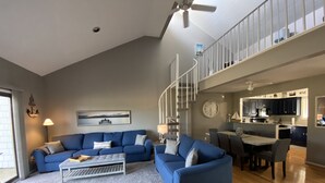 Amplia sala de estar con un conjunto de sofá azul, una mesa de centro y una escalera que lleva a un nivel superior.
