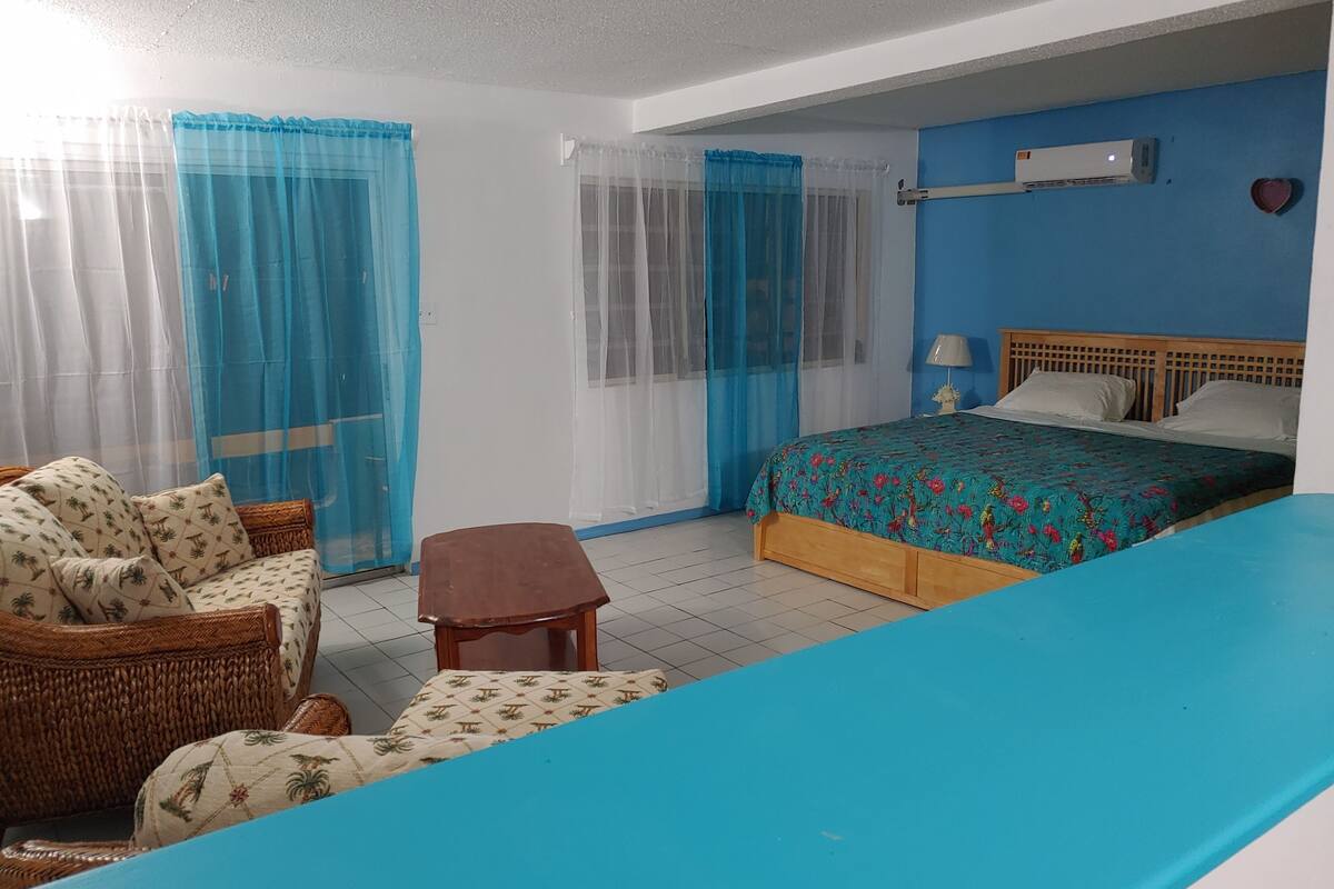 A bedroom with a bed, a small table, a wicker sofa, and a blue wall.