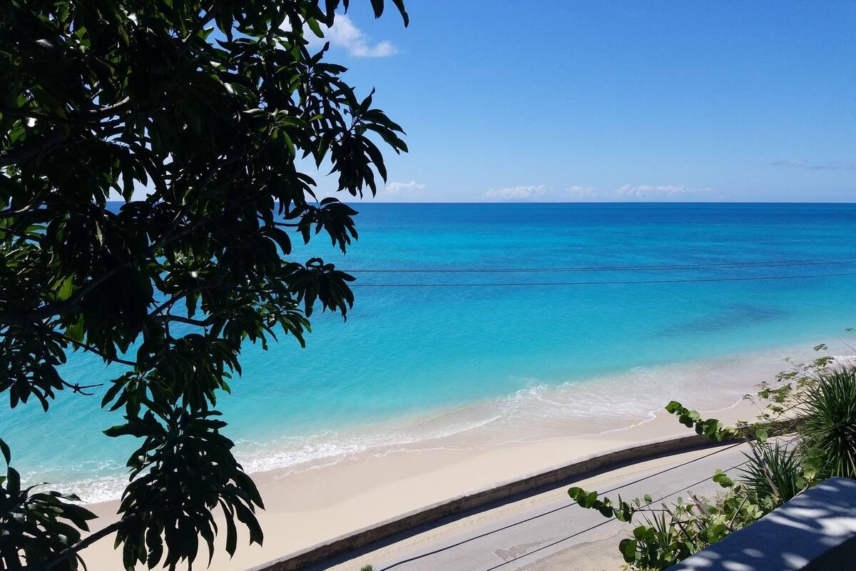 A beach with clear turquoise water, a sandy shore, and a view of the ocean.