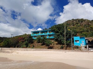 A two-story building with a balcony, situated on a hillside with a beach in the foreground. - Orrie's Beach Bar Hotel (Johnson's Point)