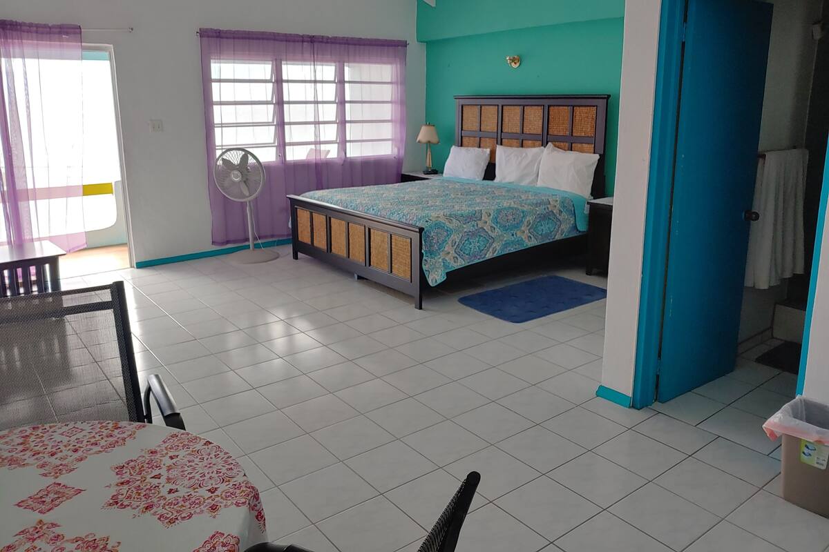 A bedroom with a bed, a fan, a table, and a chair.