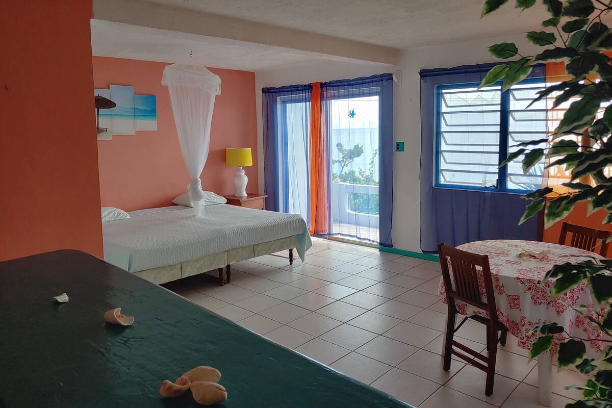 A hotel room with a bed, a table, and a chair. There is a window with curtains and a view of the outside.