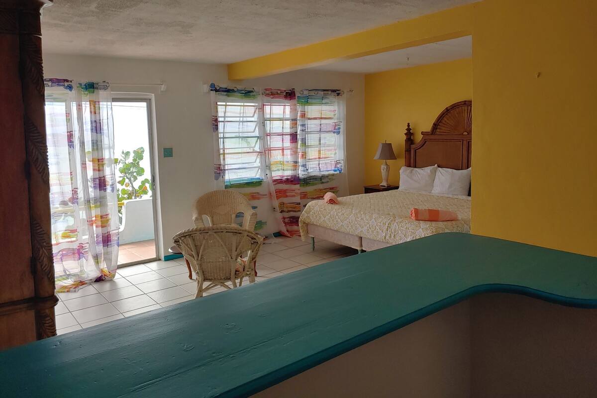 A room with a bed, a chair, a table, and a window with colorful curtains.