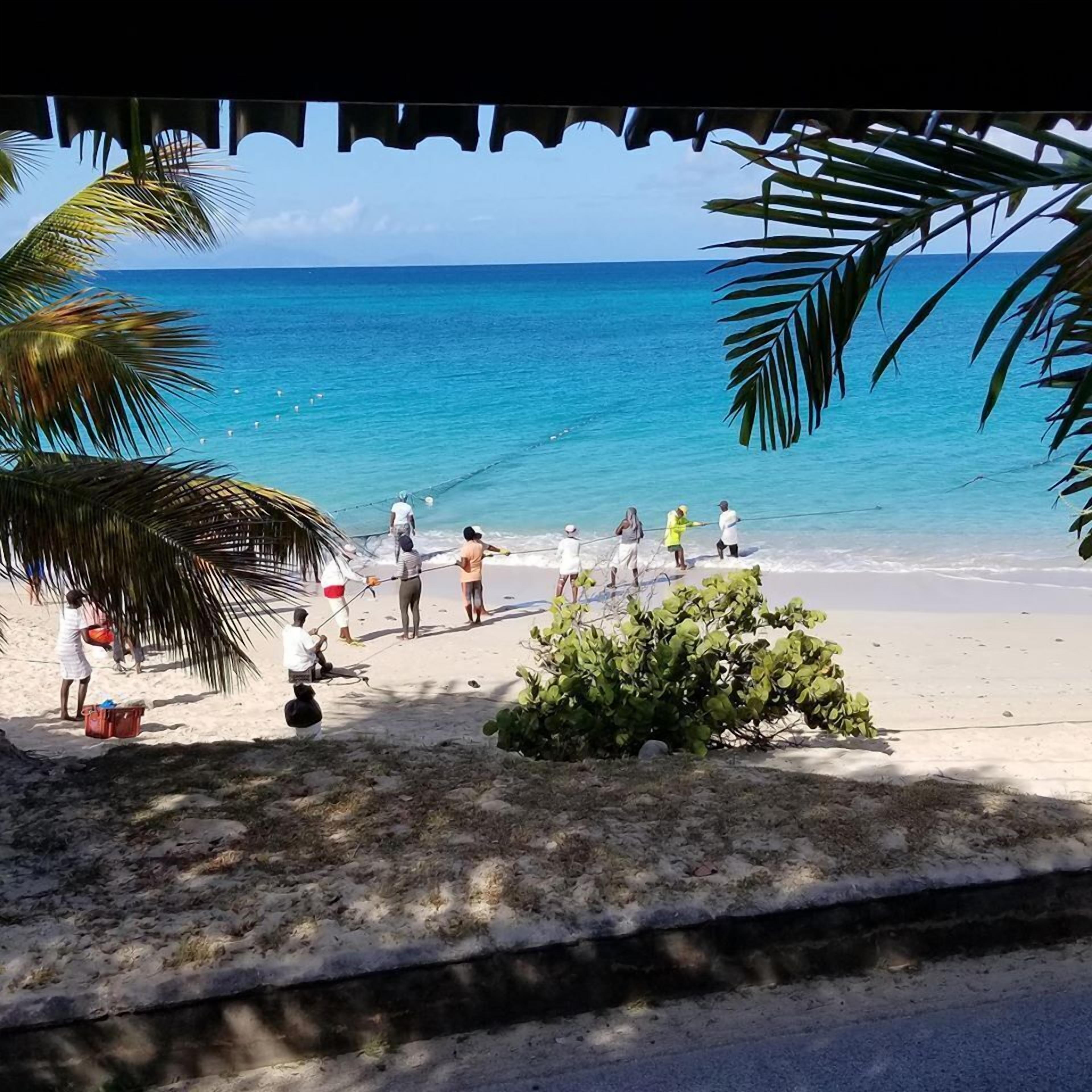 A beach scene with people fishing and a small structure with a thatched roof.