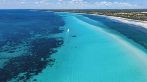An aerial view of a coastal area with clear blue waters, a sandy beach, and a distant shoreline.