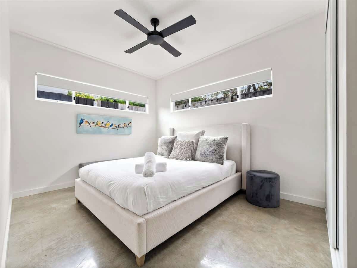 A modern bedroom with a bed, ceiling fan, built-in shelves, and a small round stool.