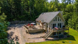 A two-story cabin with a deck, a stone wall, and a flag.