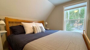 A bedroom with a large bed, a wooden headboard, and a window with a view of trees.