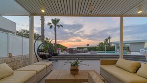 A covered outdoor seating area with wicker furniture and a view of a swimming pool and palm trees. - Venere, villa with private pool and  gym near the sea in Marina di Ragusa (Marina di Ragusa)