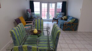 Ein Wohnzimmer mit Glastisch, gestreifter Couch und einem blauen Sofa mit gemusterten Kissen.