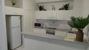 Eine Küche mit weißen Schränken, einer Mikrowelle, einem Toaster und einem Herd. Auf den Arbeitsplatten stehen Pflanzen und auf der Arbeitsfläche ein Korb.