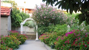 A pathway leading to a white archway surrounded by lush greenery and flowering plants. - Cosy apartment for 5 people with A/C, WIFI, TV, balcony and pets allowed (Gradac)