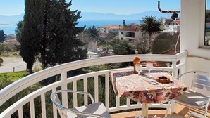 A balcony with a table and two chairs, overlooking a coastal view with buildings and trees. - Cosy apartment for 5 people with A/C, WIFI, TV, balcony and pets allowed (Gradac)