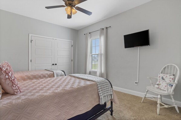 A bedroom with a bed, a chair, a TV, and a ceiling fan.