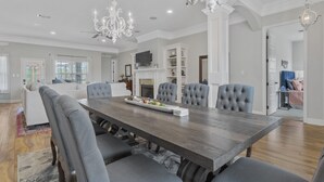 A dining area with a large wooden table, six upholstered chairs, and a chandelier. - Custom Built Lake House (Gulfport)