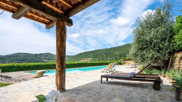 Ein Poolbereich mit einer Pergola, Liegestühlen und Blick auf die Landschaft.