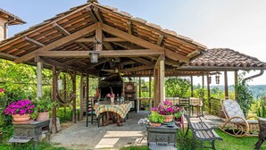Eine rustikale Terrasse im Freien mit einer Holzpergola, einem Tisch mit kariertem Tischläufer, Blumentöpfen und Gartenmöbeln.