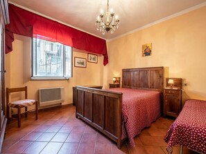 A bedroom with a large bed, a smaller bed, a chair, a radiator, a window with a view of buildings, and a chandelier. - Nice apartment in villa for 4 guests with pool, WIFI, TV, patio and pets allowed (Collina Del Negro)