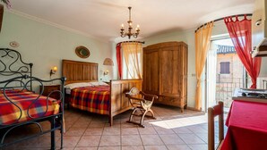 A bedroom with a bed, a chair, a wooden wardrobe, and a table with a red tablecloth.