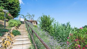 A stone staircase leading uphill with a wooden railing, surrounded by lush greenery and flowering plants.