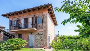 A two-story building with a balcony, stone facade, and a well-maintained garden.