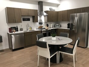 A modern kitchen with stainless steel appliances, a central island with chairs, and a 'Welcome' sign on the wall.