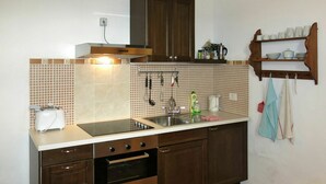 Een kleine keuken met een kookplaat, oven, spoelbak en een hangrek met keukengerei.