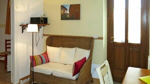 Een gezellige kamer met een rieten bank, een klein tafeltje, een lamp en een schilderij aan de muur.