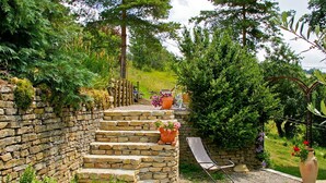 Una escalera de piedra que conduce a un jardín con macetas y una silla de metal.