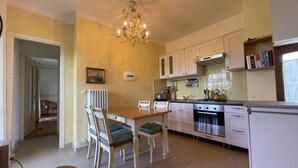 Una cocina compacta con armarios blancos, una mesa de comedor con sillas, una araña y un radiador.