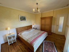 Une chambre à coucher avec un lit en bois, deux tables de chevet, un lustre, une armoire et une porte en verre dépoli.