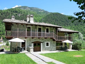 A stone building with a balcony, outdoor seating, and a mountainous backdrop. - Cosy apartment for 4 guests with WIFI, pool, TV and terrace (Sampeyre)