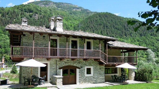 A stone building with a balcony, outdoor seating, and a mountainous backdrop. - Beautiful apartment for 4 guests with pool, WIFI, TV and terrace (Calchesio)