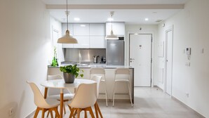A modern kitchen with white cabinets, a stainless steel refrigerator, and a dining area with a round table and chairs. - Ocean Homes Suite 2003 (Punta del Moral)
