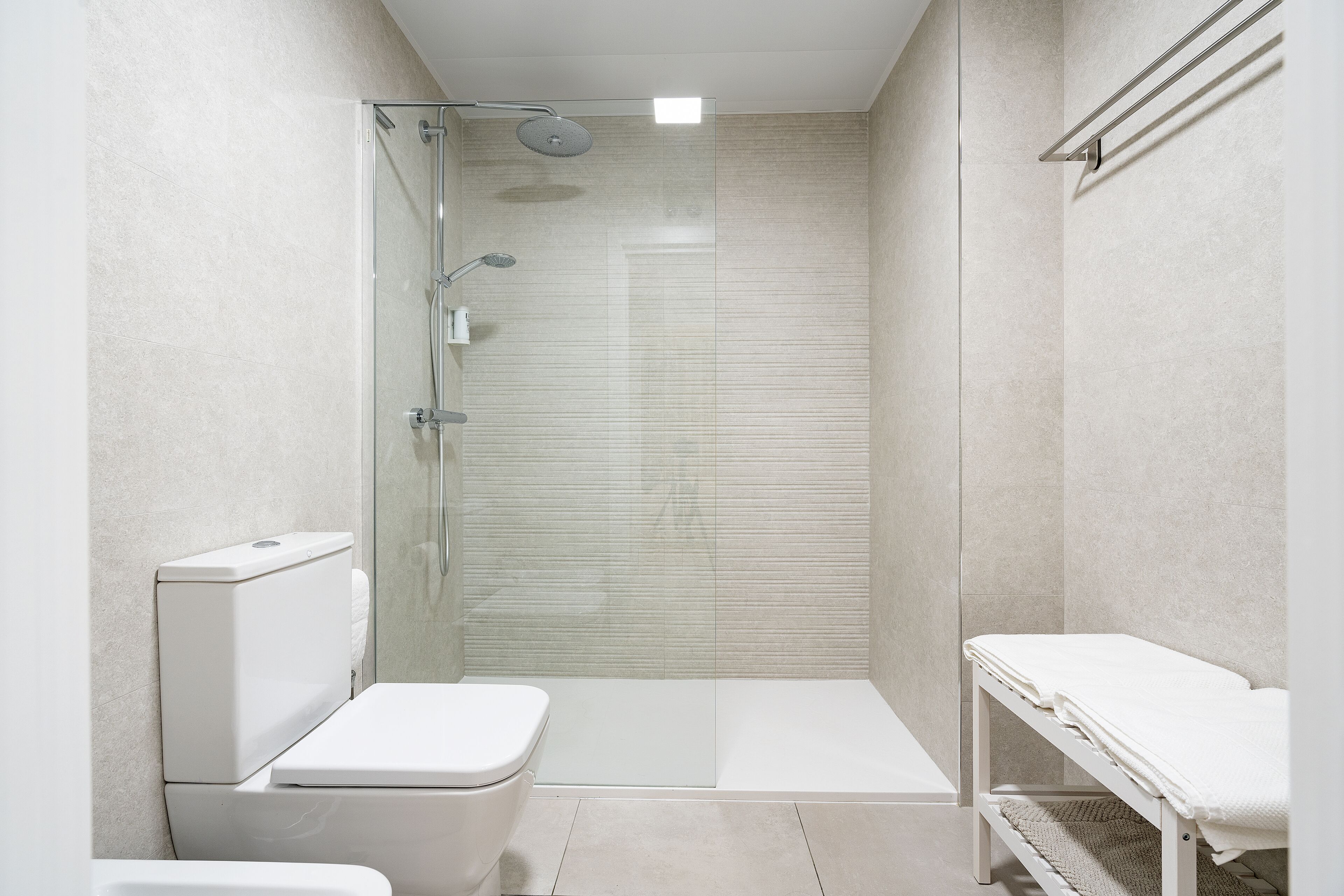 Une salle de bain moderne avec une douche à parois de verre, des toilettes et un banc.