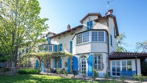 Una casa de dos pisos amb un balcó, un jardí petit i una banca blava.