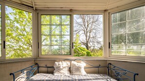 Una habitació amb llit, finestres grans i vistes als arbres.