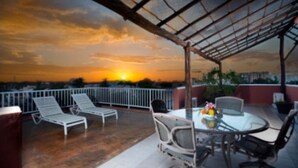A terrace with a glass table and chairs, overlooking a sunset.