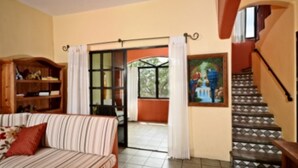 A living room with a sofa, a wooden cabinet, a staircase, and a painting on the wall.