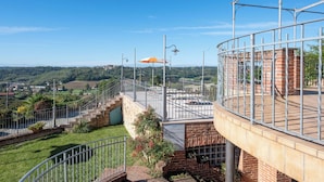Eine Dachterrasse mit Blick auf eine ländliche Landschaft, ein Backsteinhaus und ein Metallgeländer.