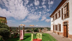 Ein Kinderspielplatz mit Rutsche und Schaukeln, ein Backsteinhaus mit Fenstern und ein klarer Himmel.