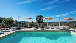 Ein Pool mit Liegestühlen und Sonnenschirmen, umgeben von einem Zaun und mit Blick auf die Landschaft.
