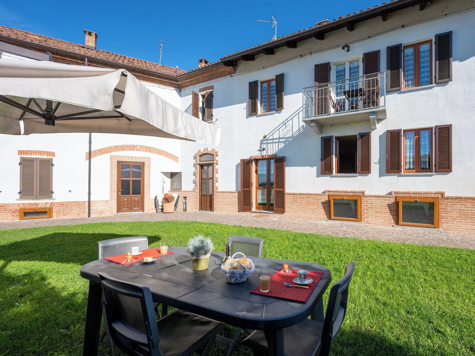 Une cour avec une table dressée pour le petit-déjeuner, entourée d’un bâtiment blanc doté de nombreuses fenêtres et d’un balcon.