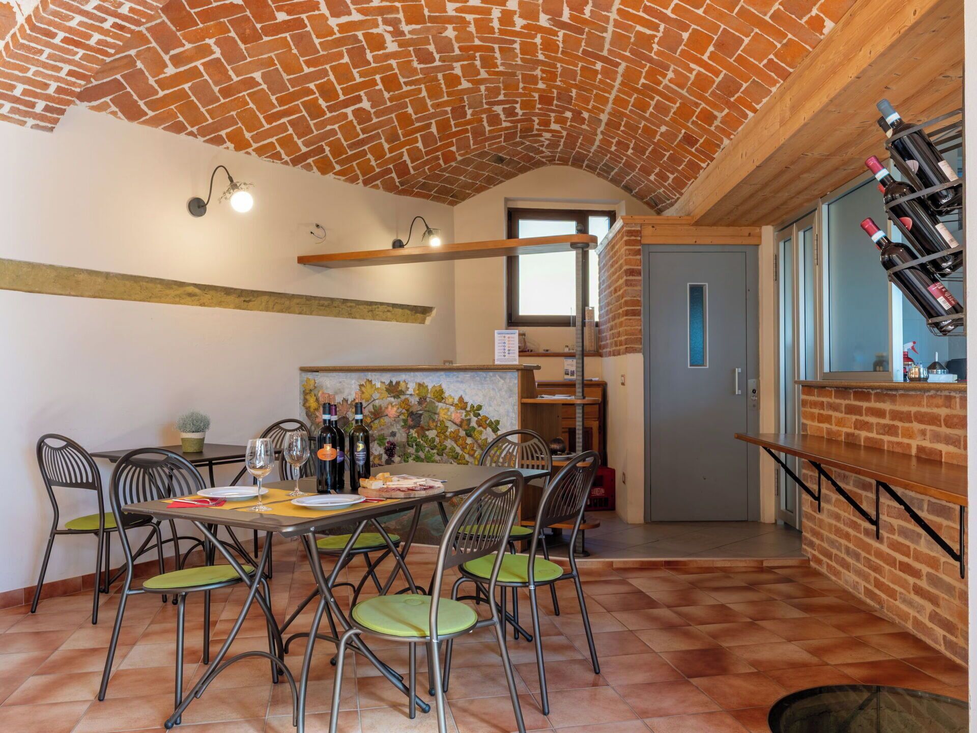 Un espace repas doté d’un plafond en briques, d’un mur en briques orné d’un motif de feuilles et d’un meuble à vin où sont rangées des bouteilles.