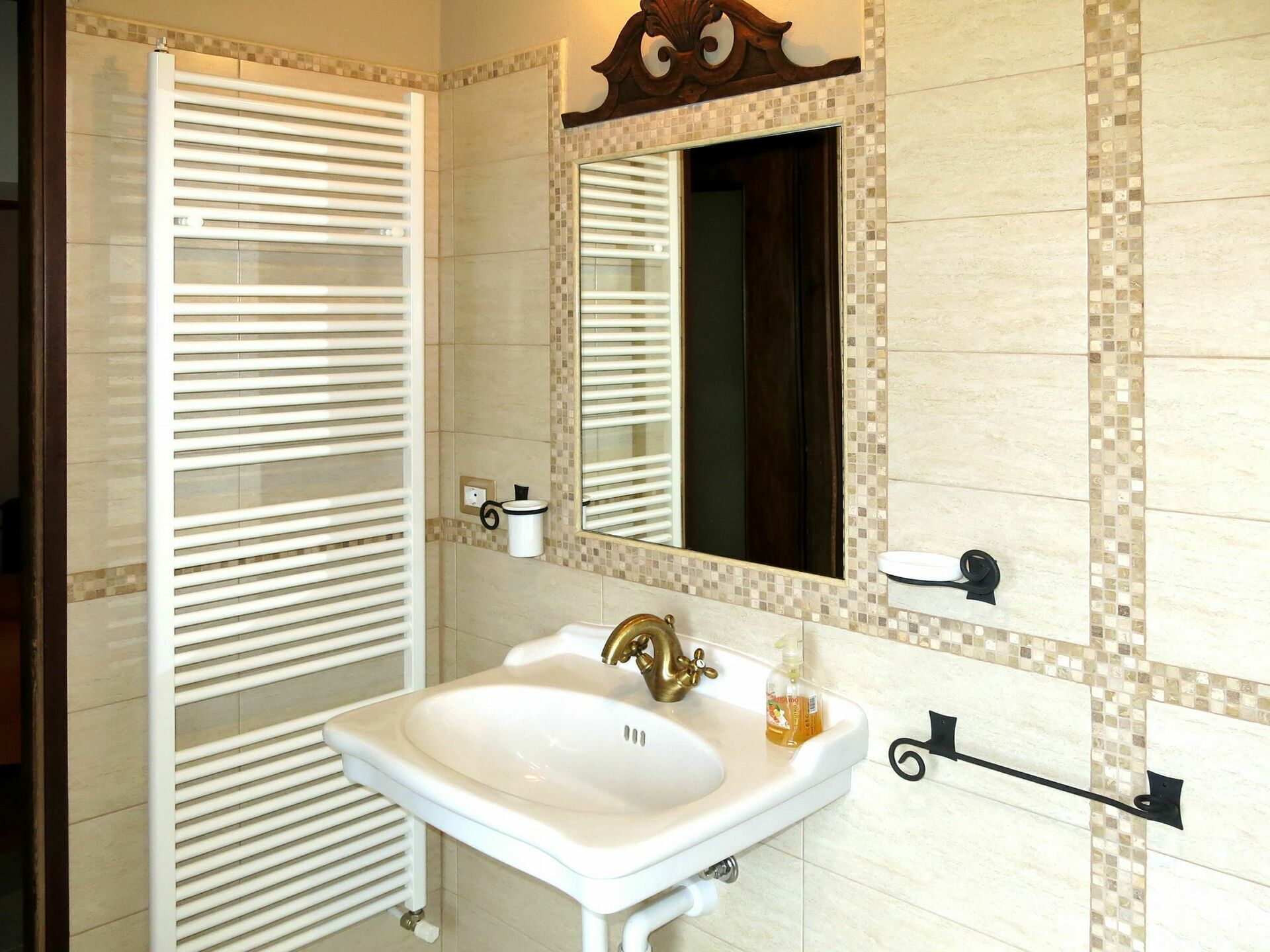 A bathroom with a white sink, a gold faucet, a mirror, and a towel rack.
