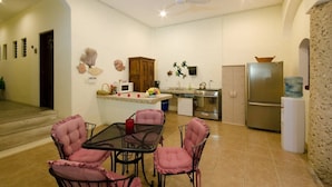 A compact kitchen with a dining area, featuring a central table with chairs, a refrigerator, and a microwave. - Summerplace Inn Condo: Colibri (San Miguel II)
