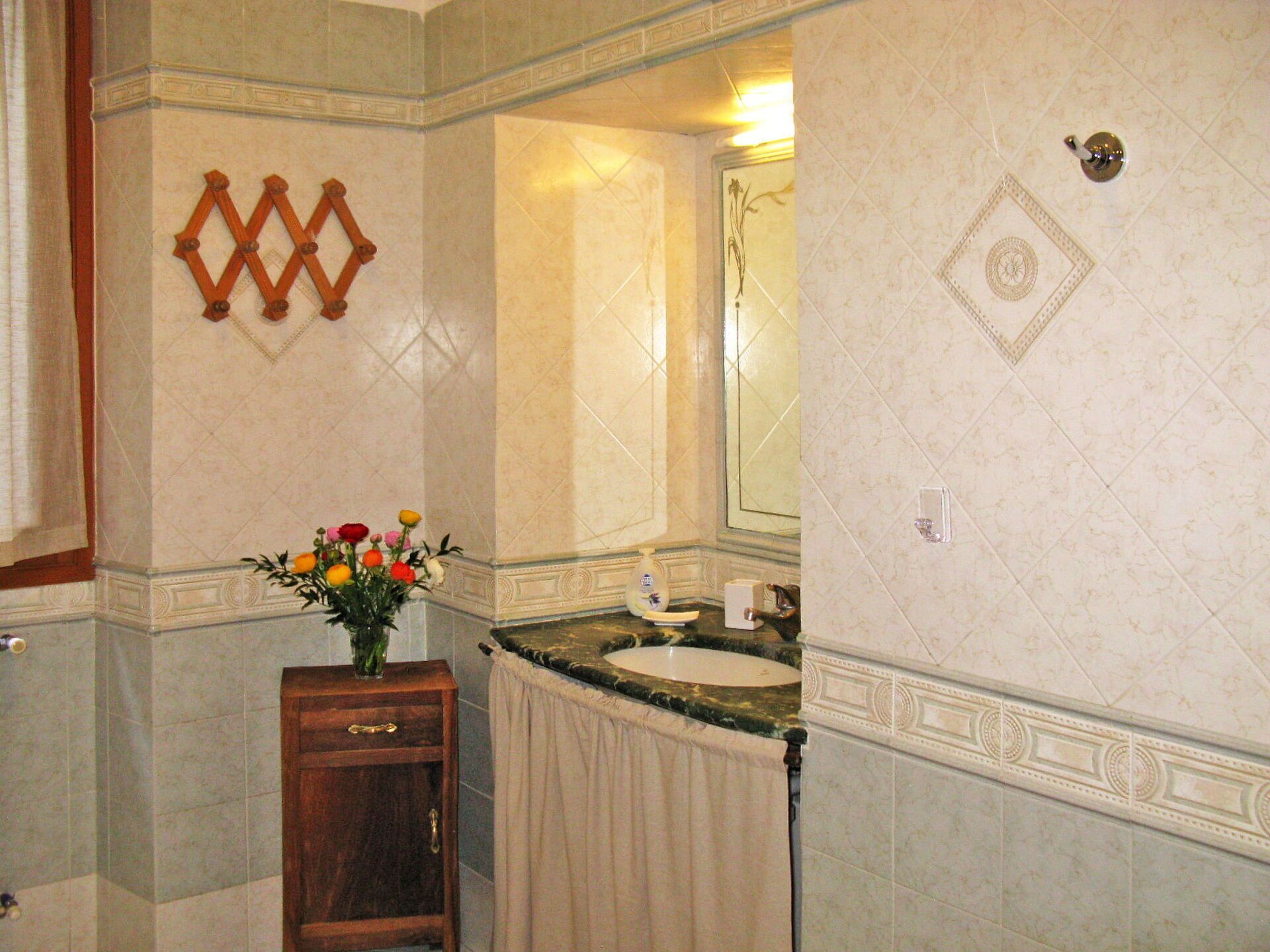 Un baño con lavamanos de mármol, un mueble de madera, un espejo y un panel decorativo en la pared.