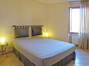 Un dormitorio con cama, dos lámparas de noche, una ventana con cortinas y un radiador.