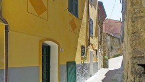 Eine enge Straße mit gelben Häusern, Steinmauern und grünen Fensterläden.